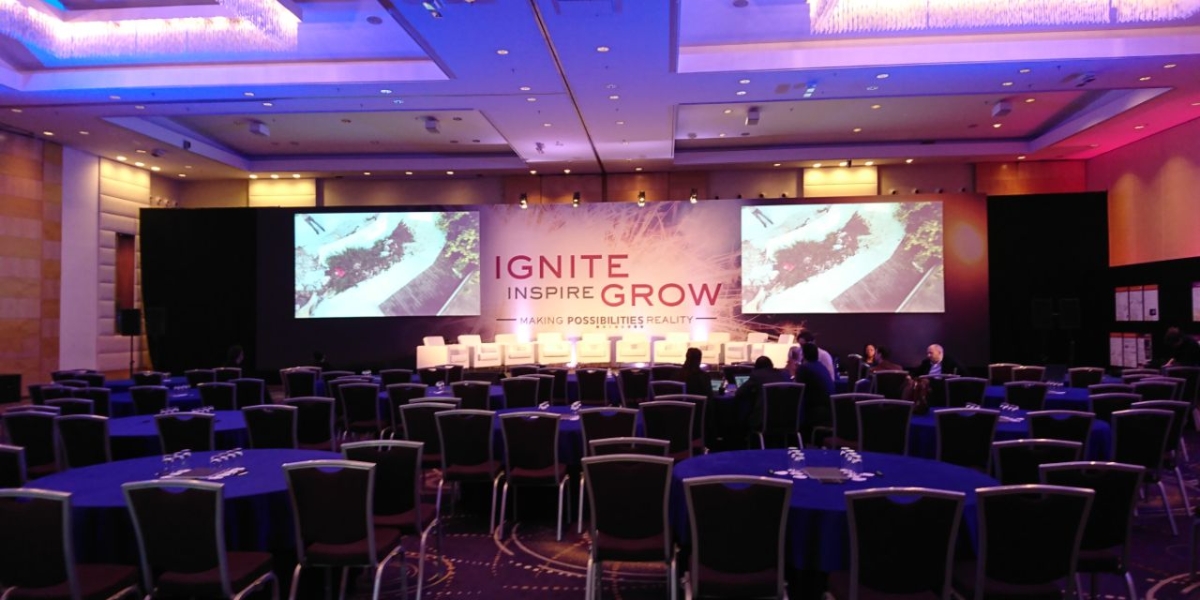 Branded backdrops for events showcased at an IGNITE conference with large projection screens displaying company messaging in a modern ballroom with blue and purple lighting.