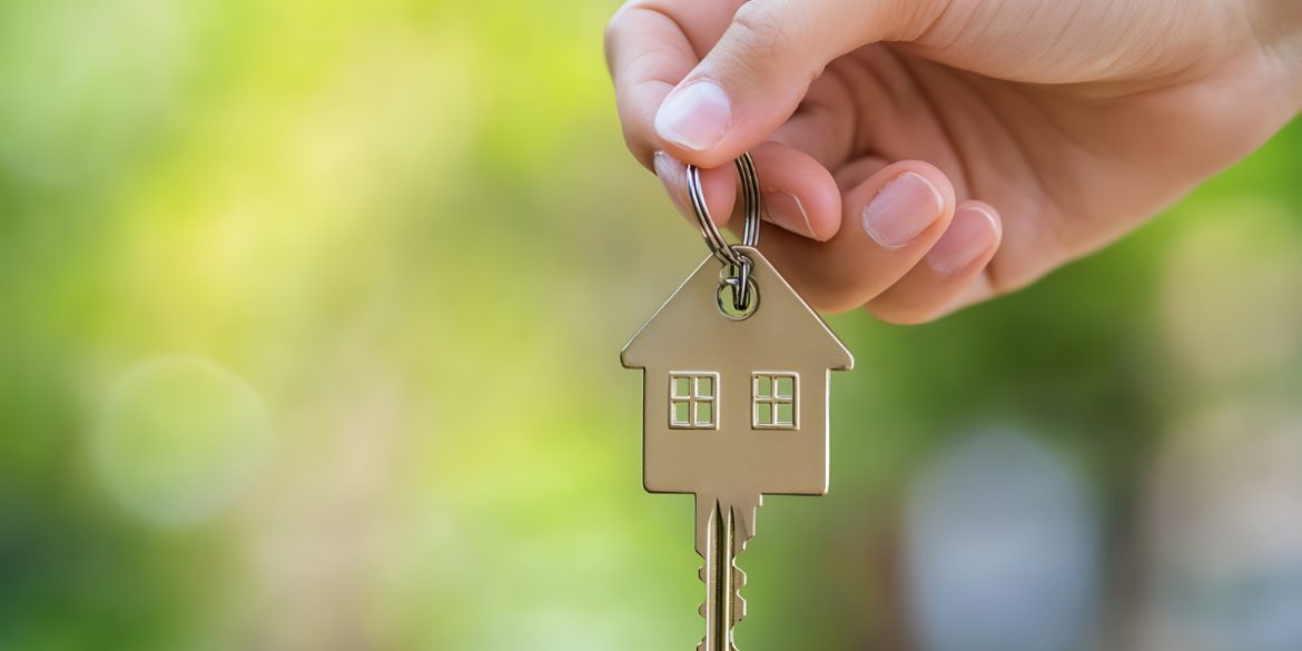 Starter home becomes a rental as hand holds house-shaped key with keychain against blurred green outdoor background
