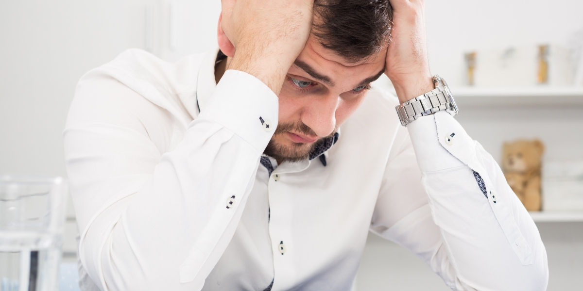 Starter home becomes a rental causing stress as young man in white shirt holds head in hands while experiencing landlord concerns
